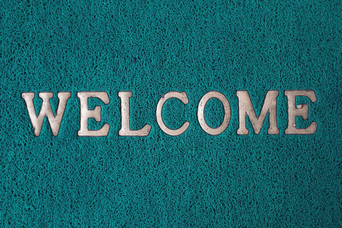 A close-up of hands placing a freshly printed, custom-designed coir doormat beside a front door, showing clear lettering and natural fiber texture — design your own doormat